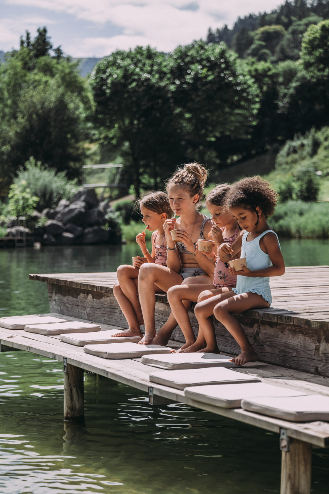 Four children eat ice cream on the wooden lake dock in summer.
