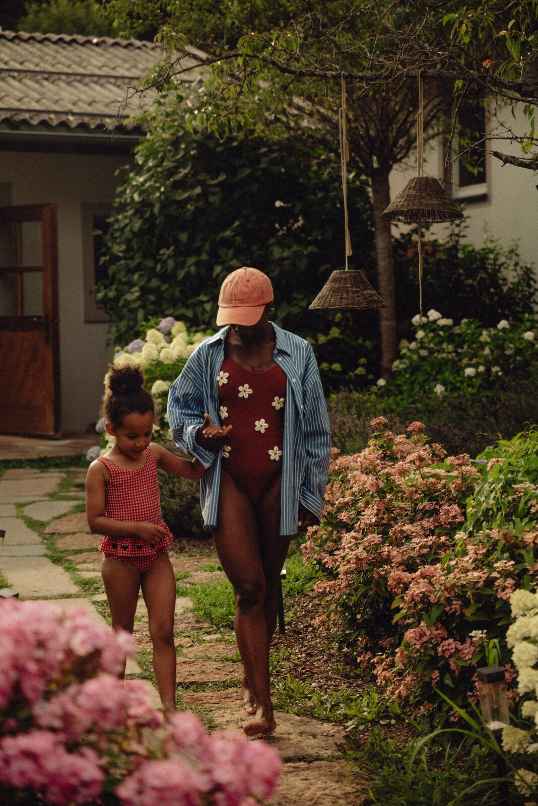Mother and daughter walk a hydrangea-lined path, barefoot.