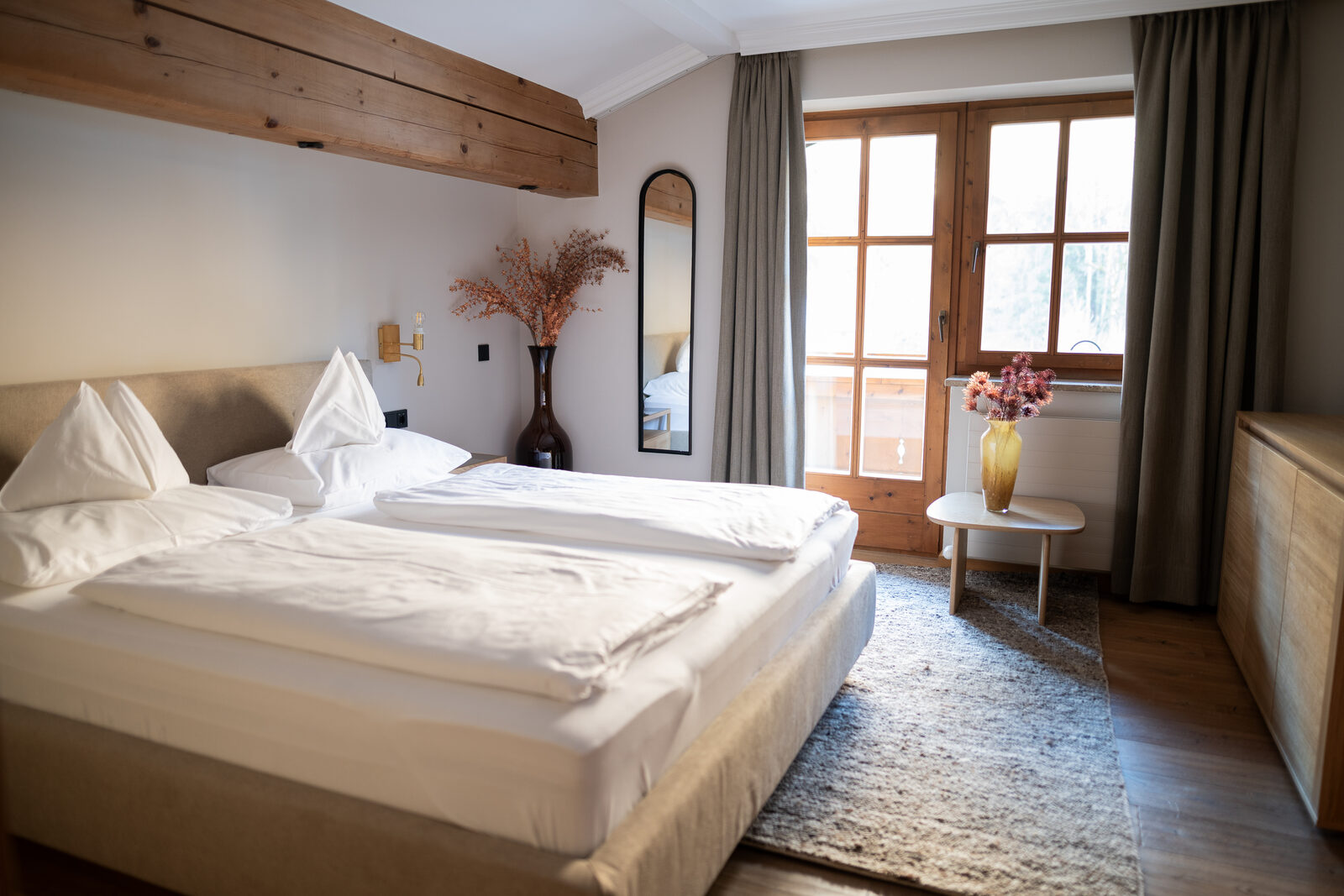 Bedroom suite with timber-beam ceiling, linen drapes and an oval mirror.