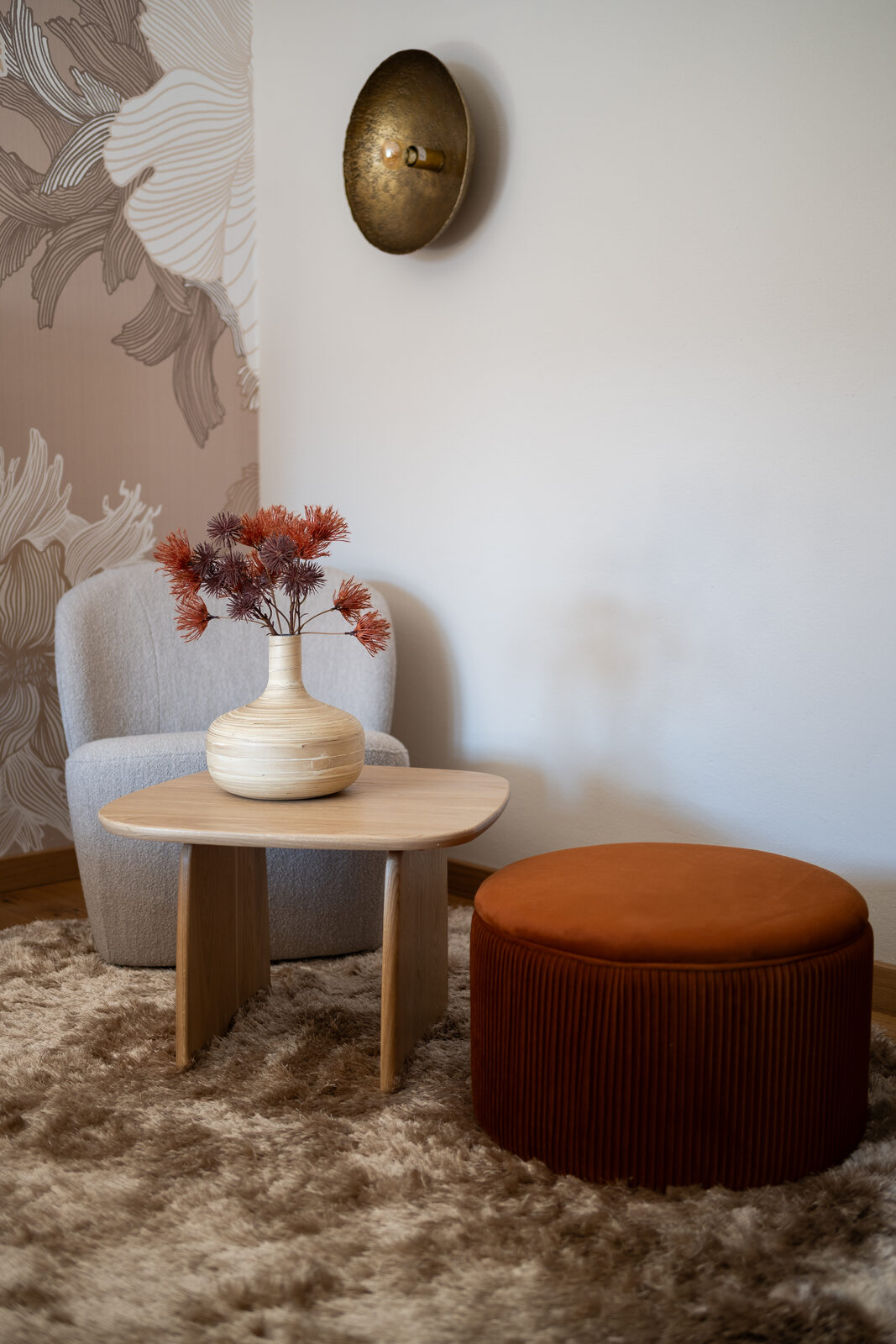 Sitting corner: gray velvet armchair, terra-cotta pouf, brass wall light.