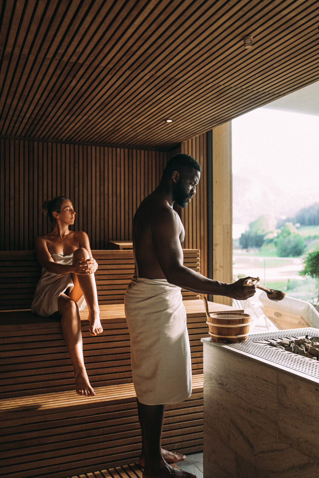 Two adults in the sauna at POST, a window onto the meadow beyond.